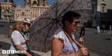 A woman with an umbrella shields herself from the sun in Prague's Old Town