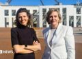 Two women standing outside federal parliament house in Canberra. One is a brunette wearing a black top and with her hands folded. The other has a short blonde bob and wearing a white blazer.