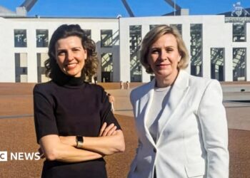 Two women standing outside federal parliament house in Canberra. One is a brunette wearing a black top and with her hands folded. The other has a short blonde bob and wearing a white blazer.