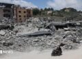 A man riding a motorcycle past destroyed buildings in the village of Mayfadoun, southern Lebanon (23 June 2026)
