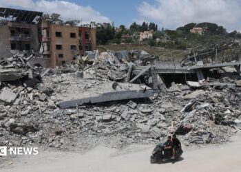 A man riding a motorcycle past destroyed buildings in the village of Mayfadoun, southern Lebanon (23 June 2026)