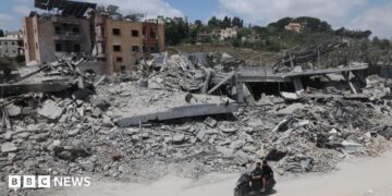 A man riding a motorcycle past destroyed buildings in the village of Mayfadoun, southern Lebanon (23 June 2026)