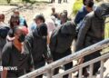 Several hooded and masked students, accompanied by adults, walk up courthouse steps under police escort