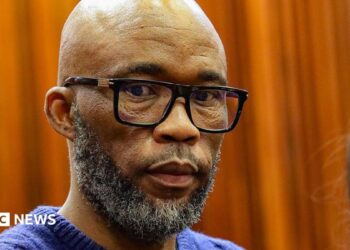 A head and shoulders picture of Cat Matlala in court - he is wearing a blue jumper, the neckline of which can just be seen at the bottom of the picture.