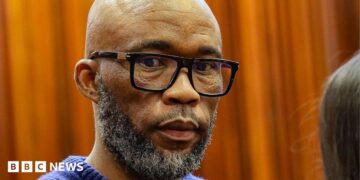 A head and shoulders picture of Cat Matlala in court - he is wearing a blue jumper, the neckline of which can just be seen at the bottom of the picture.