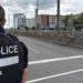 Back of officer in black vest marked with white letters reading "POLICE" next to an empty roadway with buildings across the street
