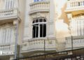 The damaged window of a light yellow residential building, which has balconies and ornate carvings.