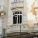 The damaged window of a light yellow residential building, which has balconies and ornate carvings.