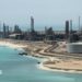 A file photo of Aramco's Ras Tanura oil refinery and oil terminal, which lies along a stretch of coast. The site comprises a network of several tall chimney-shaped structures and smaller buildings. It is daytime and the water along the coastline is a clear blue.