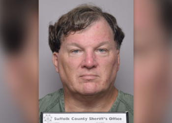 Rex Heuermann has wavy borwn hair in his latest mugshot, wearing a green shirt and holding placard that reads Suffolk County Sheriff's Office