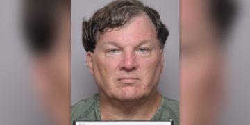Rex Heuermann has wavy borwn hair in his latest mugshot, wearing a green shirt and holding placard that reads Suffolk County Sheriff's Office