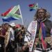 Hundreds of protesters marching outdoors, chanting and holding south african flags and signs