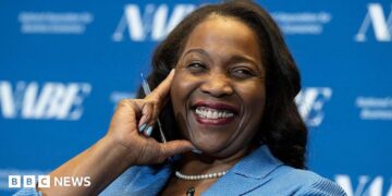Lisa D. Cook, a member of the Board of Governors of the Federal Reserve, smiles while holding her hand against her face. She is wearing a blue suit and speaks at The Capital Hilton during the 42nd annual National Association for Business Economics Economic Policy Conference on February 24, 2026 in Washington, DC.