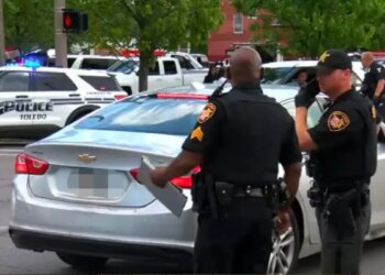 Police officers standing near vehicles at a crime scene in Toledo, Ohio