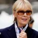 E Jean Carroll with a navy blazer, white shirt and blue patterned scarf. She is wearing large sunglasses and looking straight ahead.