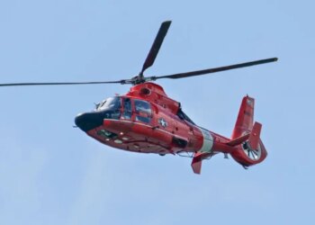 A U.S. Coast Guard Search and Rescue helicopter flying over a river area.