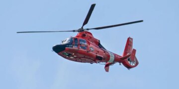 A U.S. Coast Guard Search and Rescue helicopter flying over a river area.