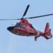 A U.S. Coast Guard Search and Rescue helicopter flying over a river area.