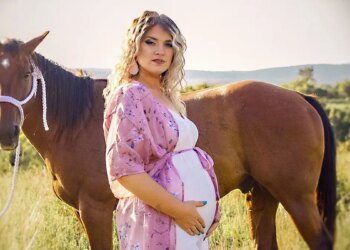 Taylor Parker in a pink gown showing off her baby bump in front of a horse.