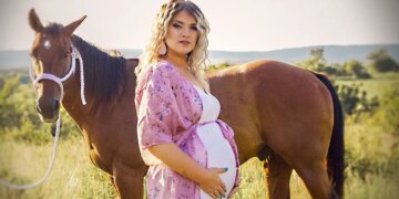 Taylor Parker in a pink gown showing off her baby bump in front of a horse.