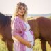 Taylor Parker in a pink gown showing off her baby bump in front of a horse.