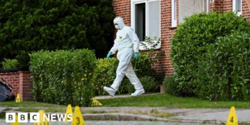 A man in a white hazmat suit walks out of a house in Stade, Germany.