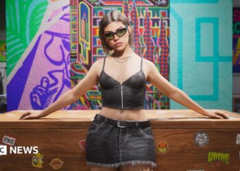 An in-game screenshot from GTA 6 showing a woman inside a shop in a short black top and a skirt with her arms resting on a desk behind her and a colourful background. She is wearing black sunglasses and has short brown hair.