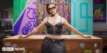 An in-game screenshot from GTA 6 showing a woman inside a shop in a short black top and a skirt with her arms resting on a desk behind her and a colourful background. She is wearing black sunglasses and has short brown hair.