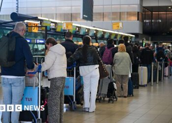 People wait at the top of escalators with luggage and checking phones at the Eurostar terminal at St Pancras in London, in December. The Eurostar sign can be seen in the background.