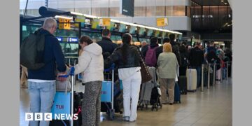 People wait at the top of escalators with luggage and checking phones at the Eurostar terminal at St Pancras in London, in December. The Eurostar sign can be seen in the background.