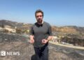 Nick Beake in a black shirt standing in the aftermath of wildfire.