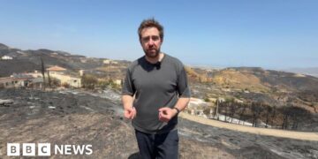 Nick Beake in a black shirt standing in the aftermath of wildfire.