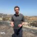 Nick Beake in a black shirt standing in the aftermath of wildfire.
