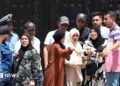Police stand guard at a black gates of an orphanage in Algiers as a crowd of men and women gesticulate outside