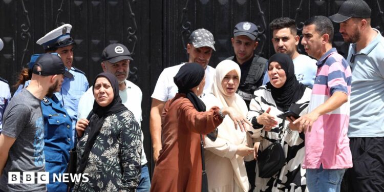 Police stand guard at a black gates of an orphanage in Algiers as a crowd of men and women gesticulate outside
