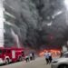 Plumes of black smoke and flames can be seen as a fire truck sprays a burning building with water