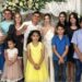 Twelve family members smile at the camera while what appears to be a bride and groom hold up their traditional wedding ring fingers