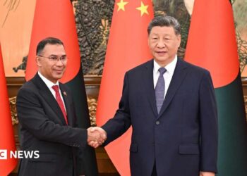 Bangladesh PM Tarique (left) and Chinese President Xi Jinping shaking hands. Behind them there are flags of both countries.