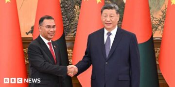 Bangladesh PM Tarique (left) and Chinese President Xi Jinping shaking hands. Behind them there are flags of both countries.