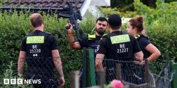 Four police officers are pictured, with one officers holding a gun up