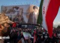 an Iranian security officer amid crowds in front of a billboard showing the late supreme leader at his funeral