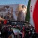 an Iranian security officer amid crowds in front of a billboard showing the late supreme leader at his funeral