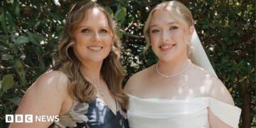 Hannah and her mother at Hannah's wedding. Her mother is wearing a blue dress with white flowers. Hannah on the right is dressed in a white wedding dress holding a bouquet