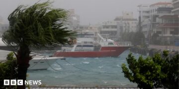 High winds and wet weather at a marina in Ishigaki Island, in Japan's Okinawa Prefecture. Wind blows through a palm tree and boats are seen on a choppy sea close to the quay.