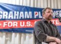 Graham Platner stands in front of a sign for his candidacy