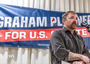 Graham Platner stands in front of a sign for his candidacy