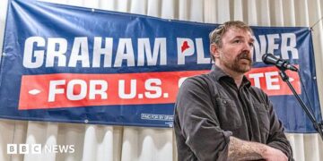 Graham Platner stands in front of a sign for his candidacy