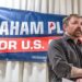 Graham Platner stands in front of a sign for his candidacy