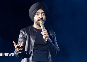 Diljit Dosanjh kicks off his Aura World Tour at BC Place on April 23, 2026, in Vancouver, British Columbia, Canada. He is wearing a black jacket over a black t-shirt and sporting a black turban, as he speaks on a microphone from the stage.
