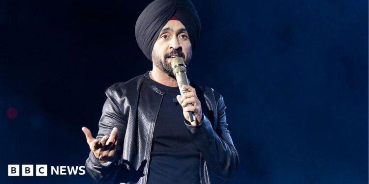 Diljit Dosanjh kicks off his Aura World Tour at BC Place on April 23, 2026, in Vancouver, British Columbia, Canada. He is wearing a black jacket over a black t-shirt and sporting a black turban, as he speaks on a microphone from the stage.